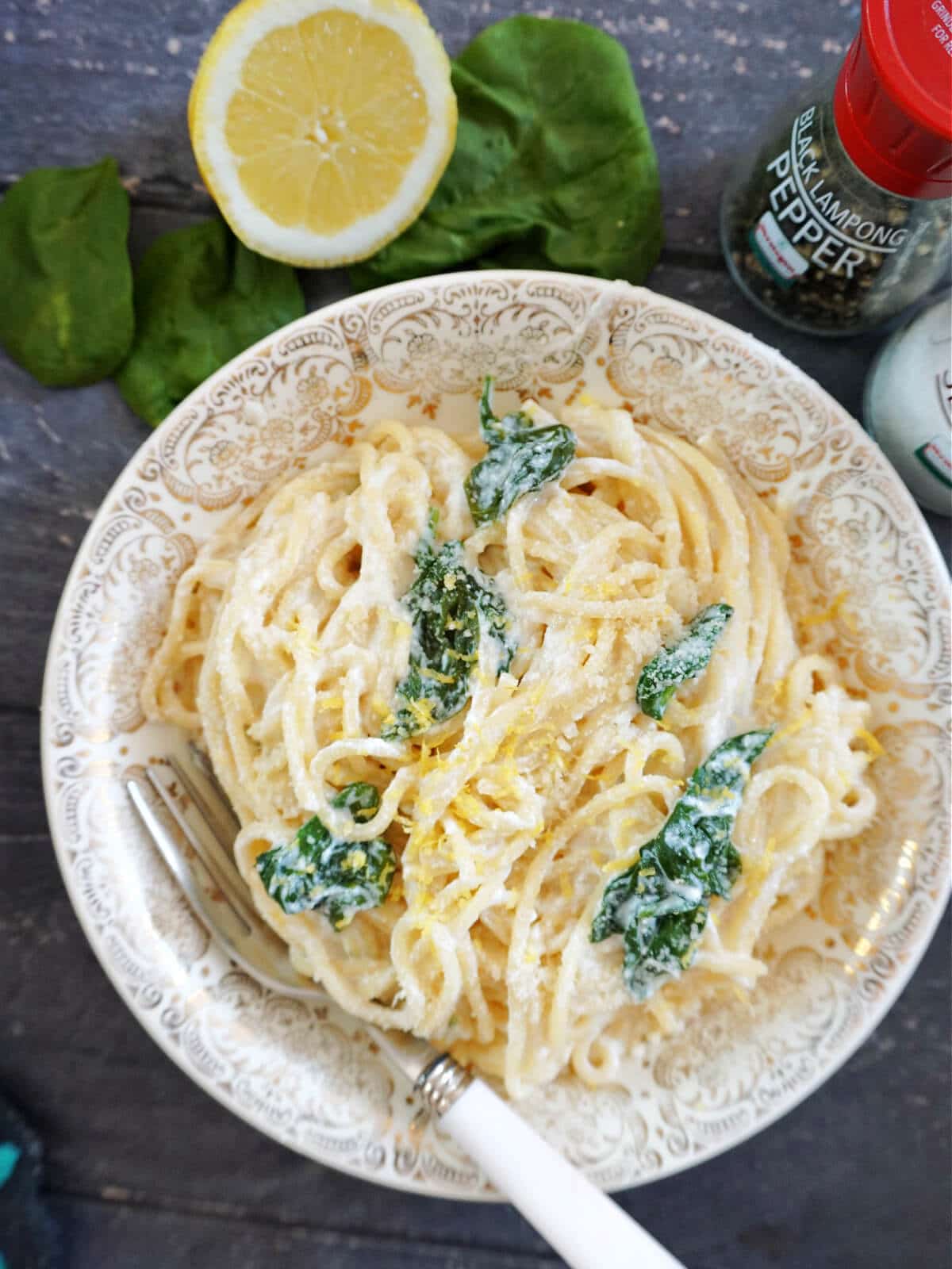 Overhead shot of a bowl of pasta with spinach and lemon, and half a lemon plus spinach leaves on the outside