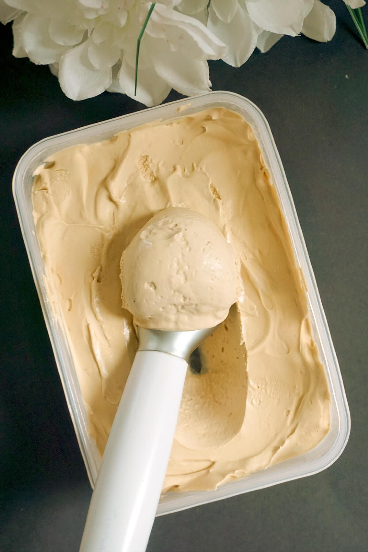 Overhead shoot of a container with coffee ice cream and an ice cream scoop.