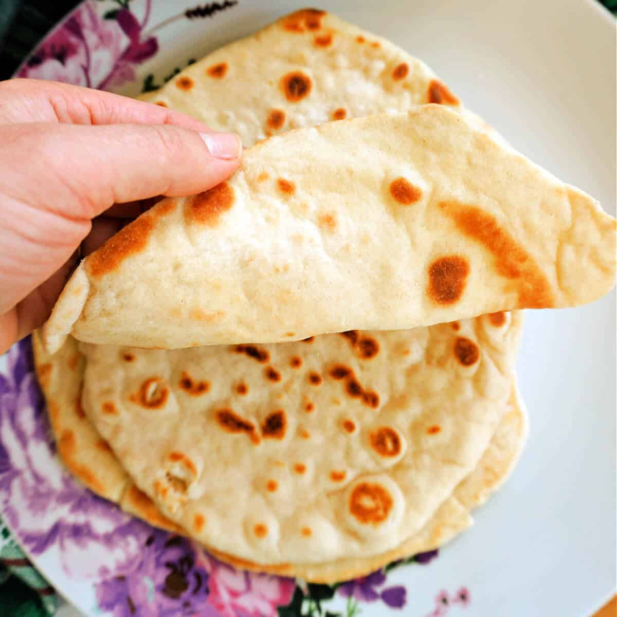 A hand showing a pile of flatbreads on a plate.