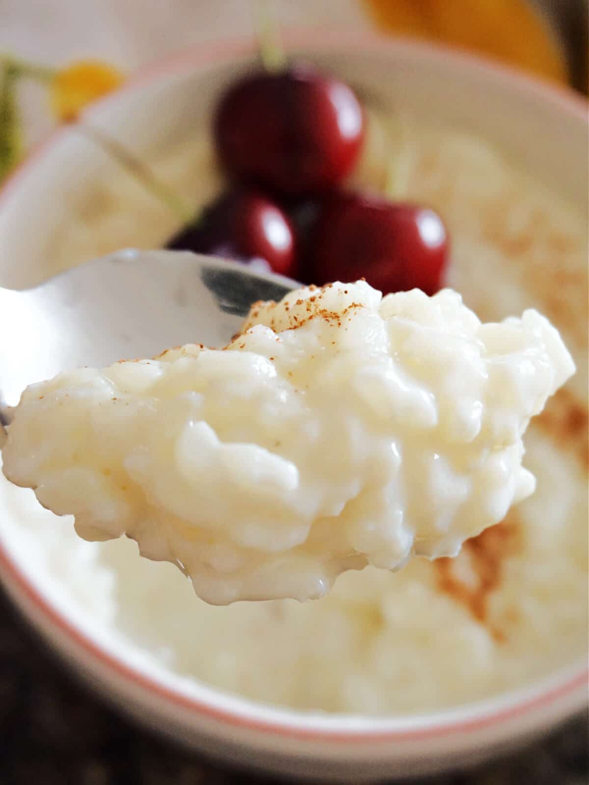 A spoonful of rice pudding over a bowl with more pudding and 3 cherries.