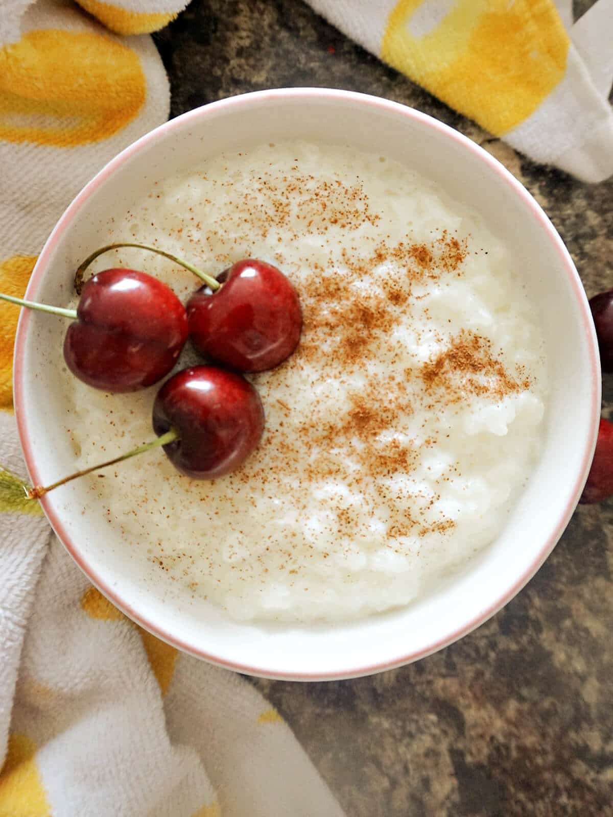 Overhead shot of a white bowl with rice pudding and 3 cherries.