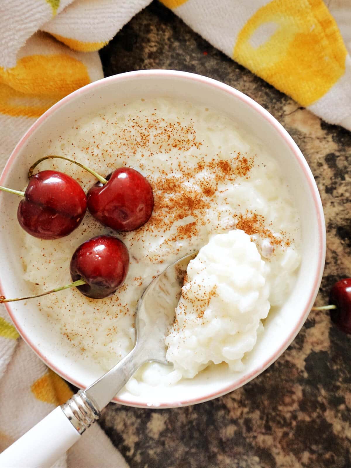 Overhead shot of a white bowl with rice pudding and 3 cherries.