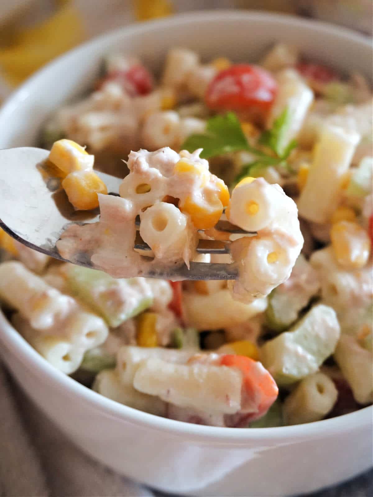 Close-up shot of a white bowl with tuna pasta salad and a fork in it.