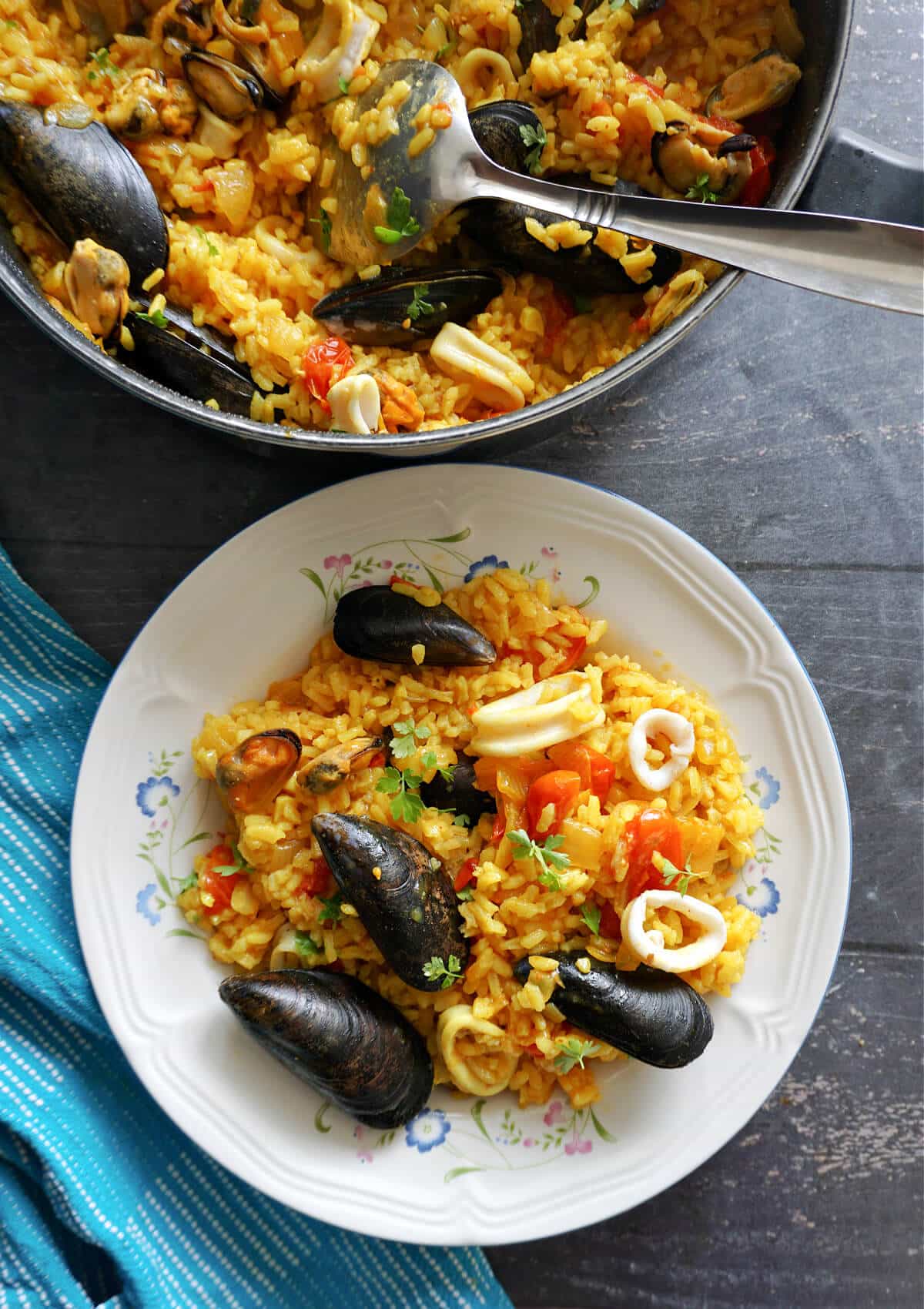 Overhead shot of a white plate with seafood yellow rice and a pot next to it with more rice.