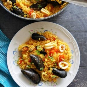 Overhead shot of a white plate with seafood paella and a pan with more rice