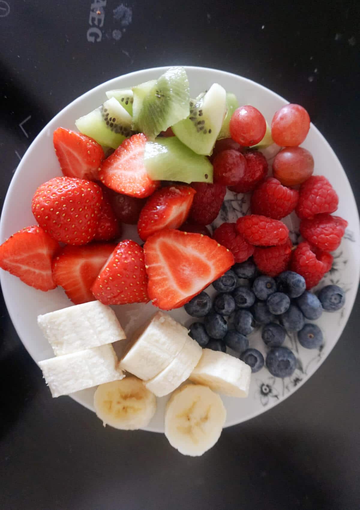 Overhead shot of a plate with chunks of fresh berries, bananas and kiwis.
