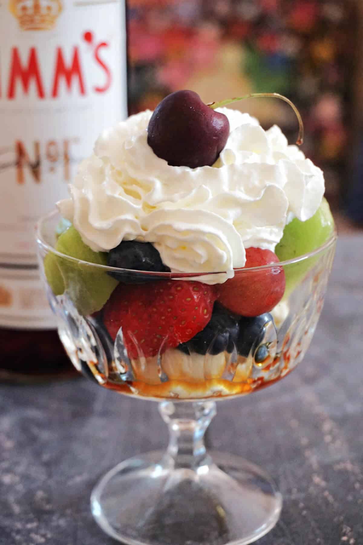 A glass with fruit salad topped with squirty cream.