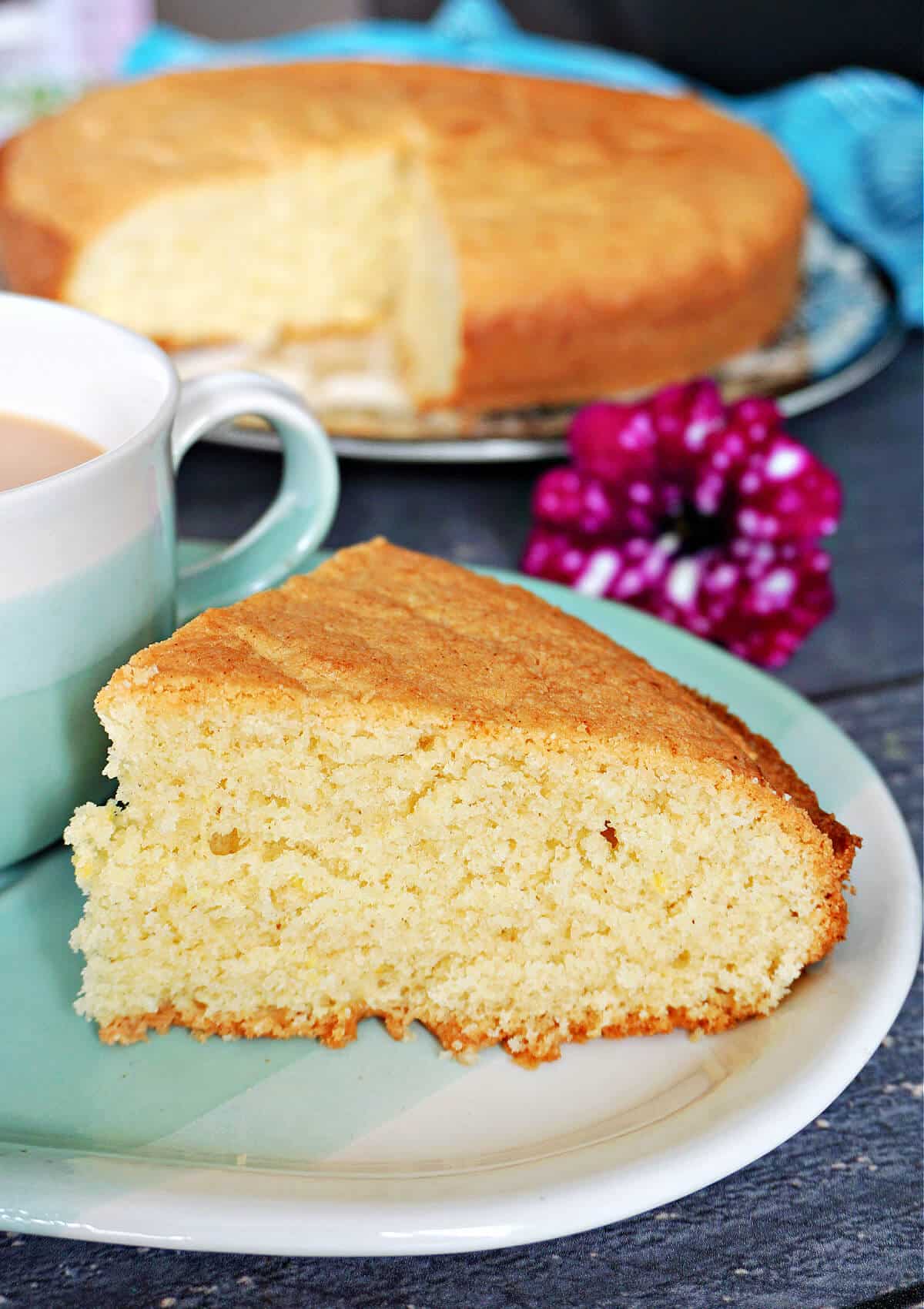 A slice of cake on a blue plate next to a cup of tea with more cake in the background