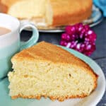 A slice of madeira cake on a blue plate with more cake in the blackground