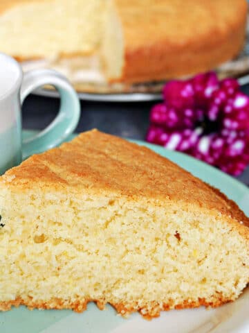 A slice of madeira cake on a blue plate with more cake in the blackground