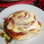 A cinnamon roll topped with cream cheese icing on a white plate