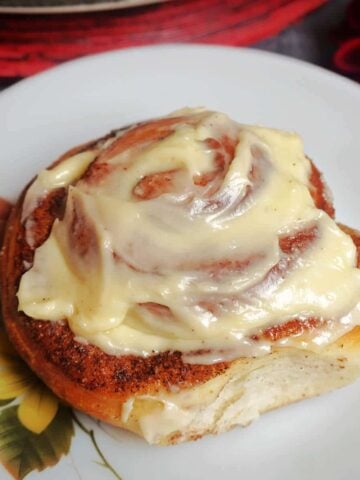 A cinnamon roll topped with cream cheese icing on a white plate