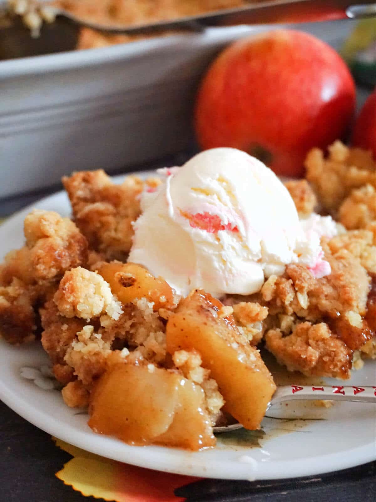 Close-up shoot of a portion of apple crumble topped with a scoop of ice cream on a white plate