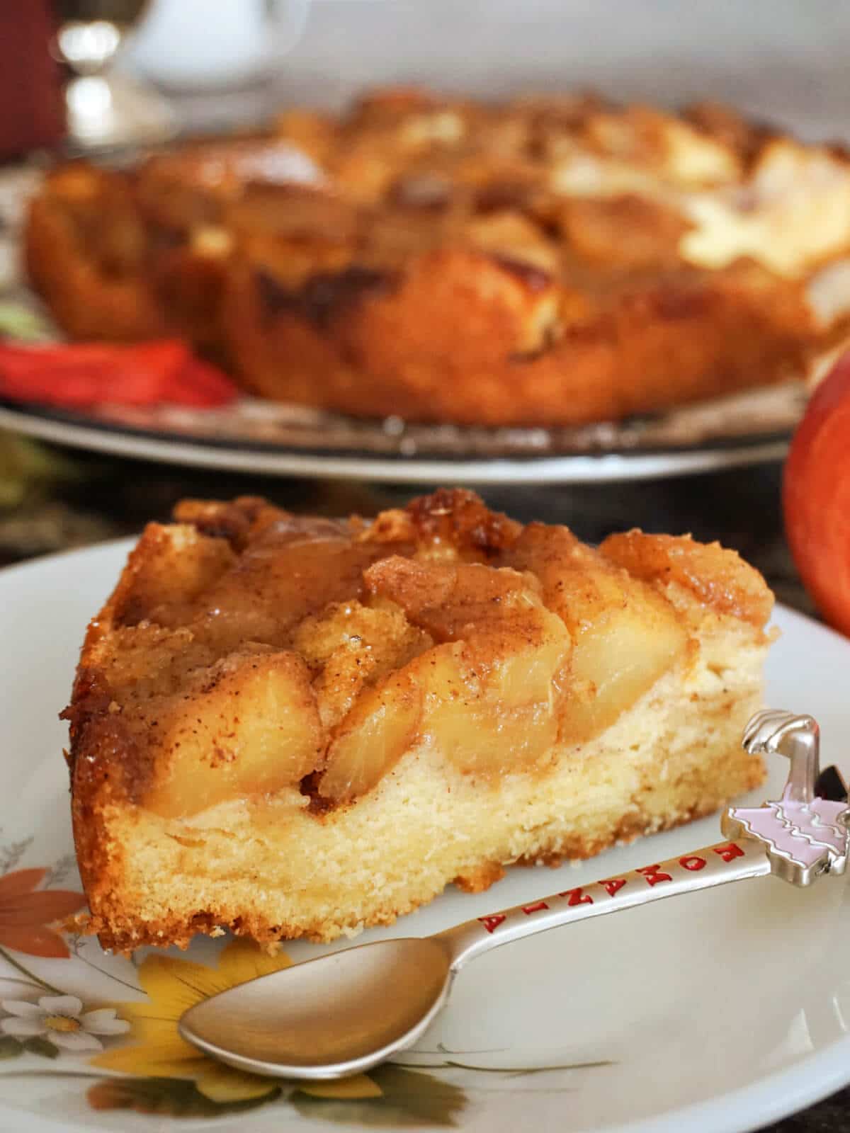 A slice of apple cake on a white plate with more cake in the background.