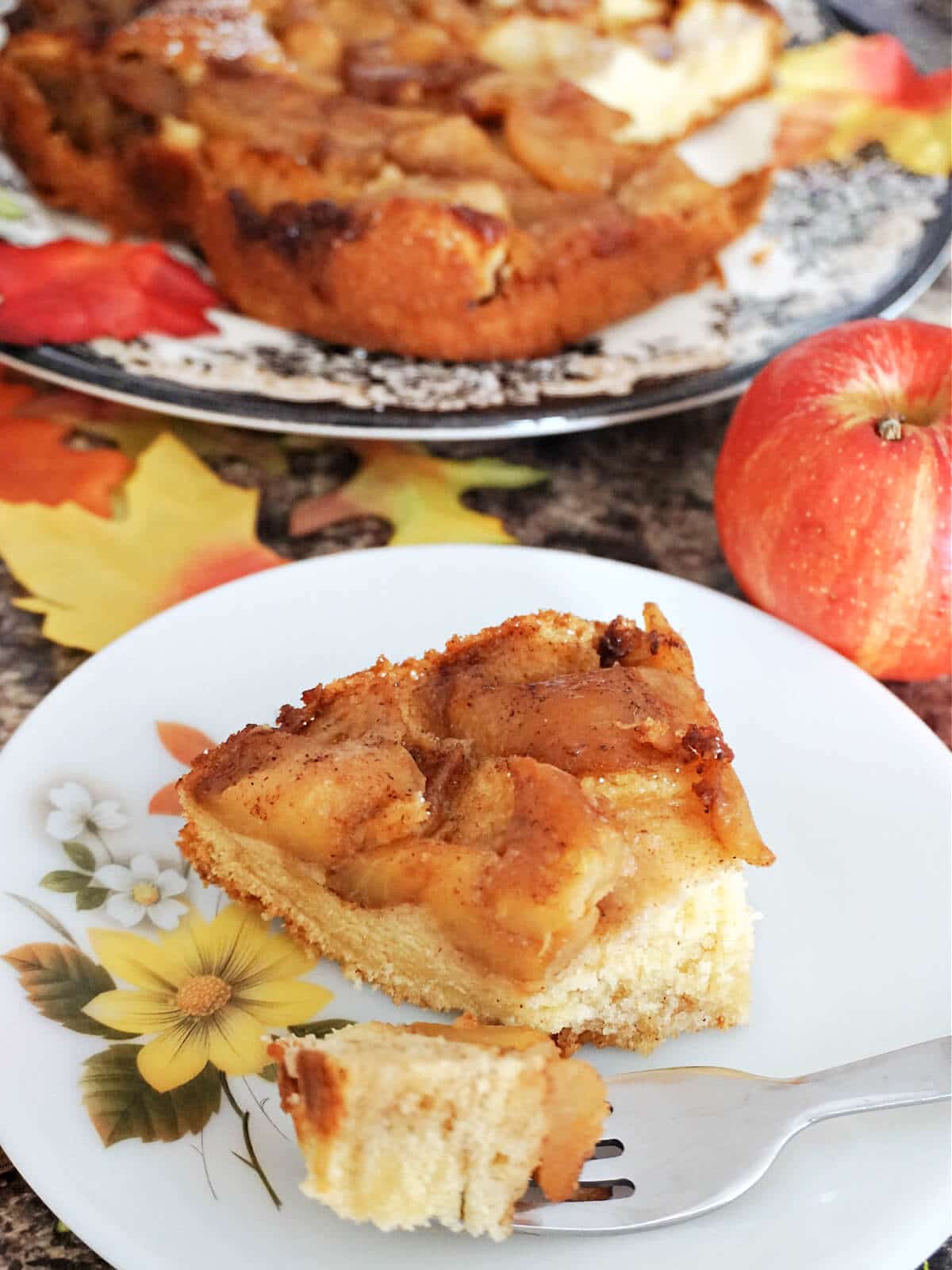 A slice of apple cake on a white plate with more cake in the background.