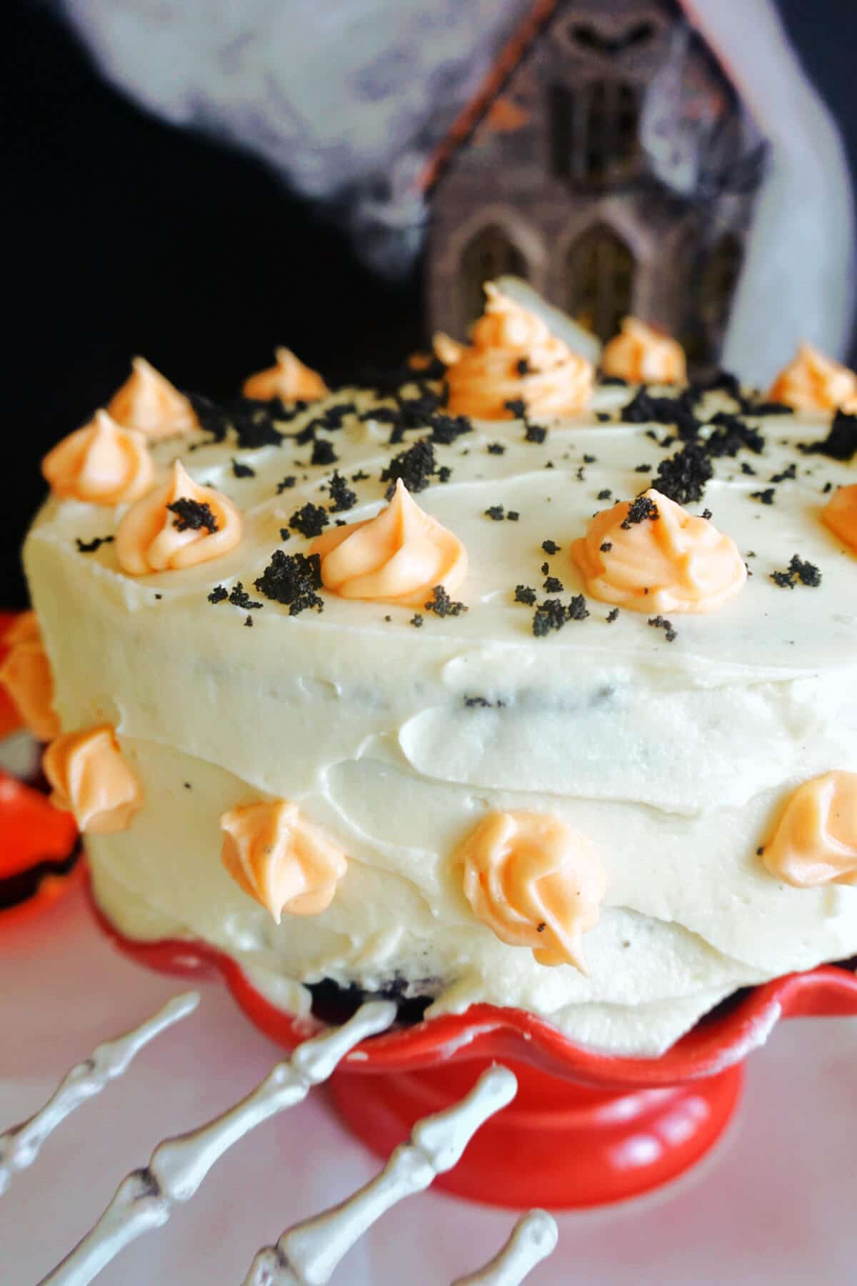 A black velvet cake covered with white buttercream frosting and decorated with orange cream swirls.