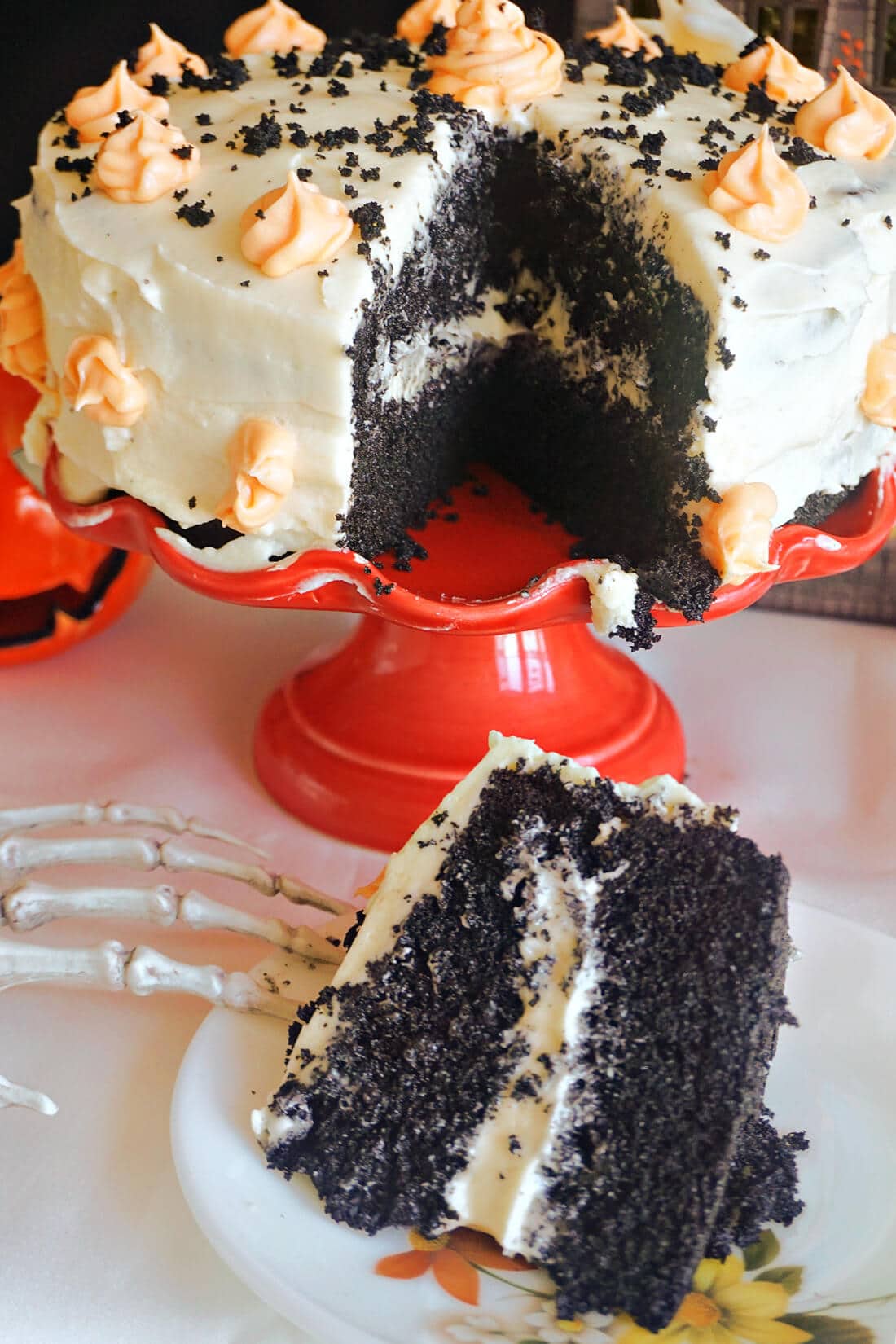 A slice of black velvet cake on a white plate with a cake stand with more cake in the background.