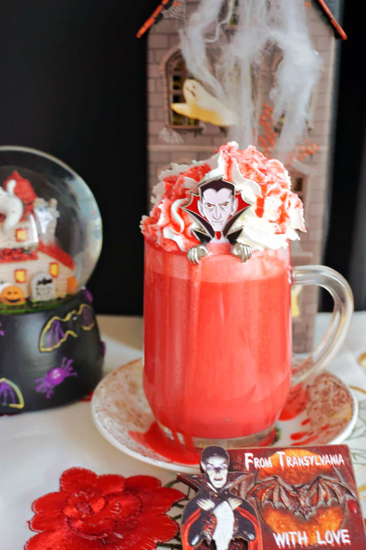 A glass of red hot chocolate with Halloween decorations around.
