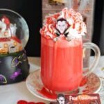 A glass of red hot chocolate topped with cream and halloween decorations around