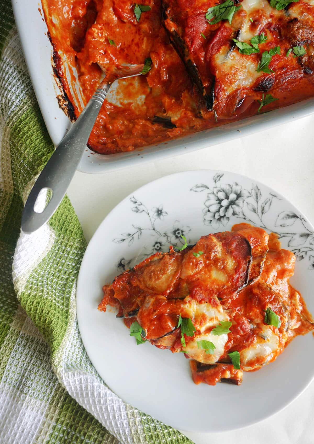 Overhead shoot of a white plate with a portion of aubergine parmesan and a dish with more aubergine.