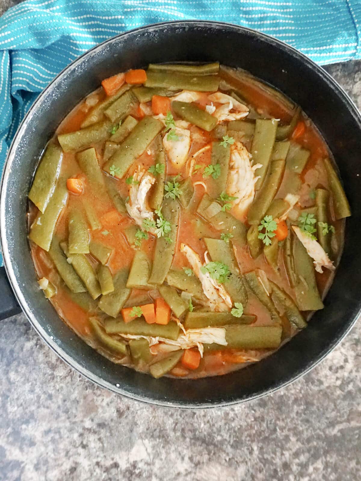 Overhead shoot of a pan with green bean stew with shredded chicken pieces.