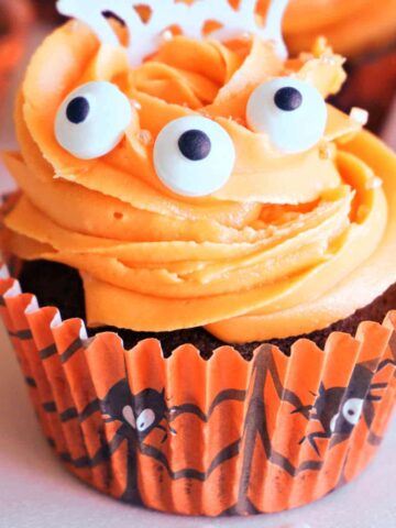 A Halloween cupcake with orange frosting and 3 edible eyes