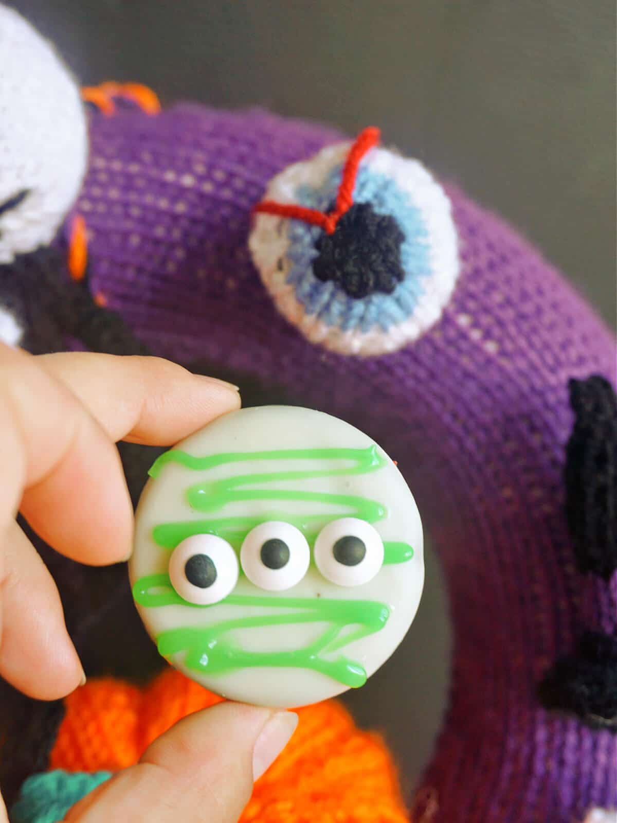 A monster cookie with a knitted Halloween wreath in the background.