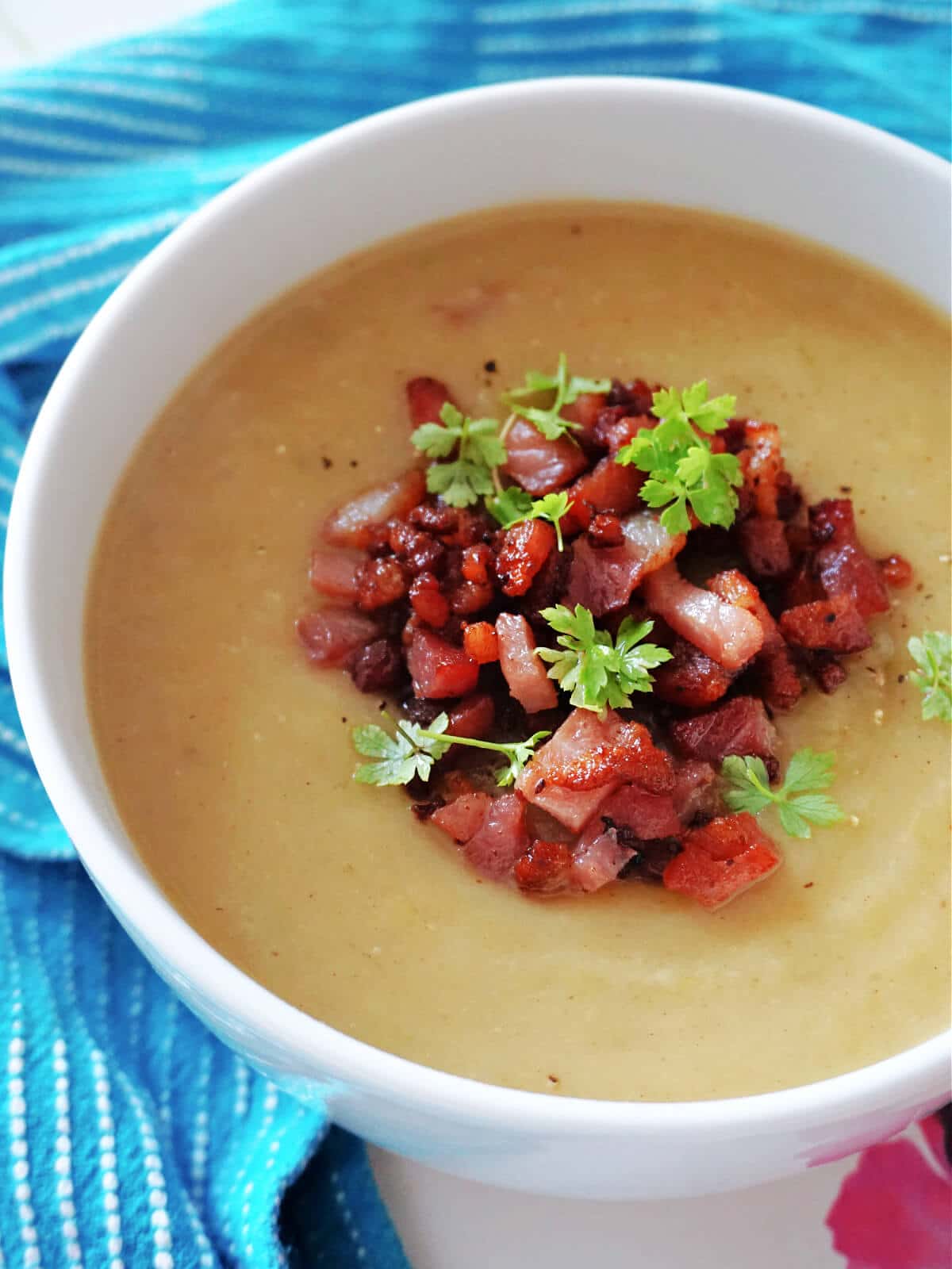 A white bowl with leek and potato soup topped with bacon bites and fresh parsley.