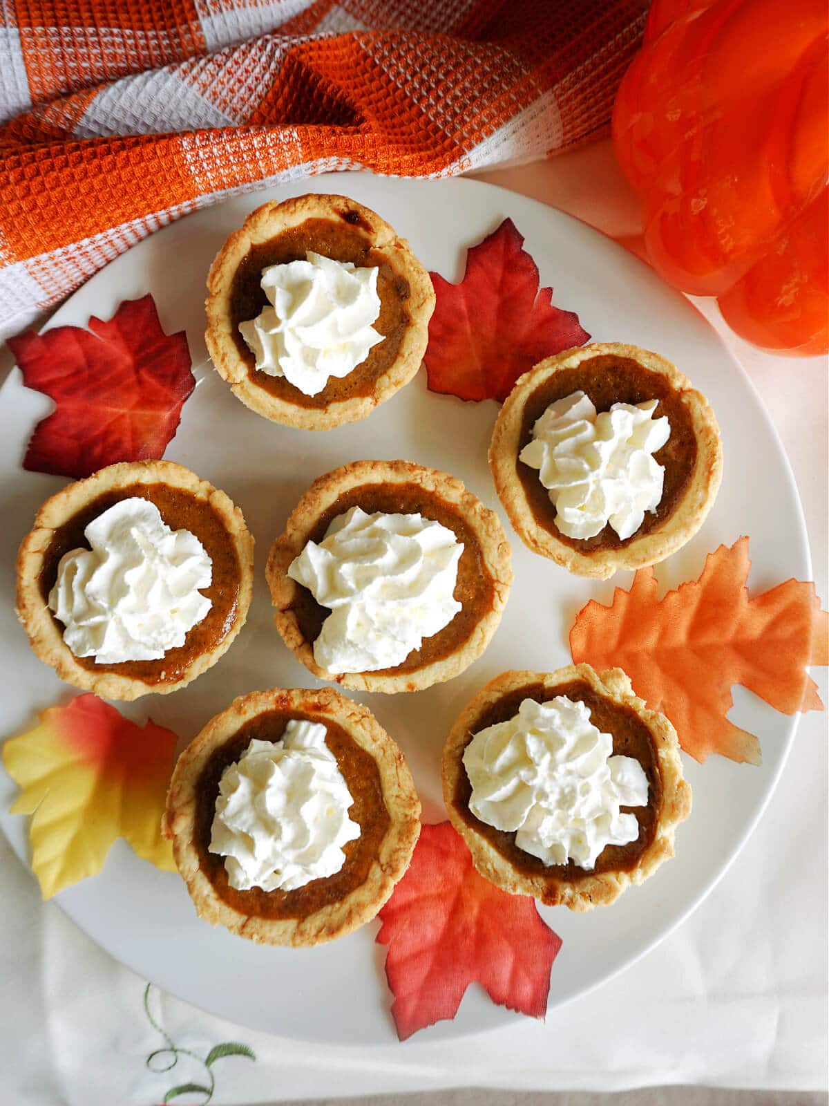 Overhead shoot of a white plate with 6 mini pumpkin pies and decorating leaves.