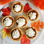 Overhead shoot of a white plate with 6 mini pumpkin pies topped with whipped cream and decorative leaves around