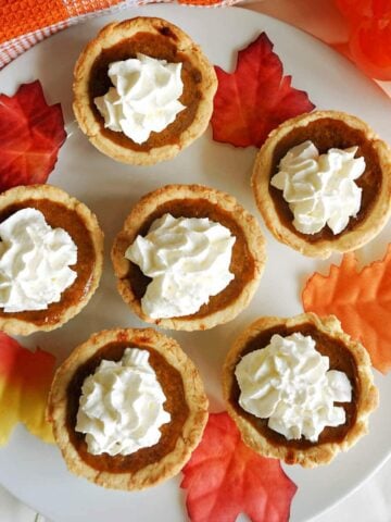 Overhead shoot of a white plate with 6 mini pumpkin pies topped with whipped cream and decorative leaves around