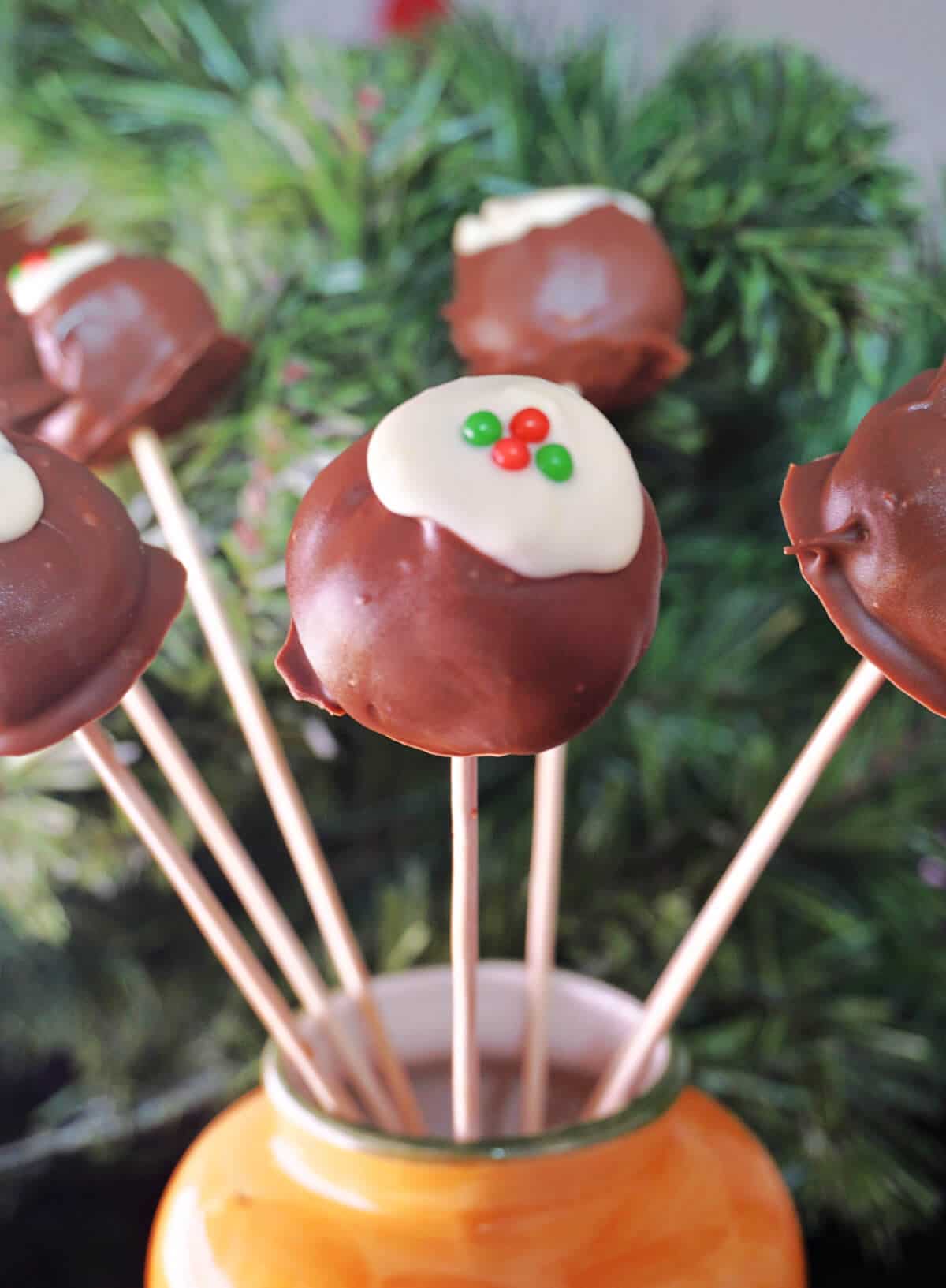 6 christmas pudding cake pops with a christmas tree in the background.