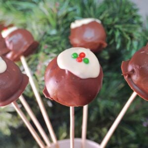 A jug with 6 Christmas pudding cake pops and a christmas tree in the background