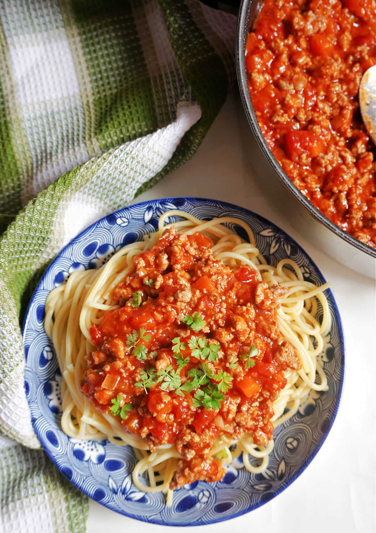 Overhead shoot of a blue plate with spaghetti and turkey bolognese, and a dish with more sauce.