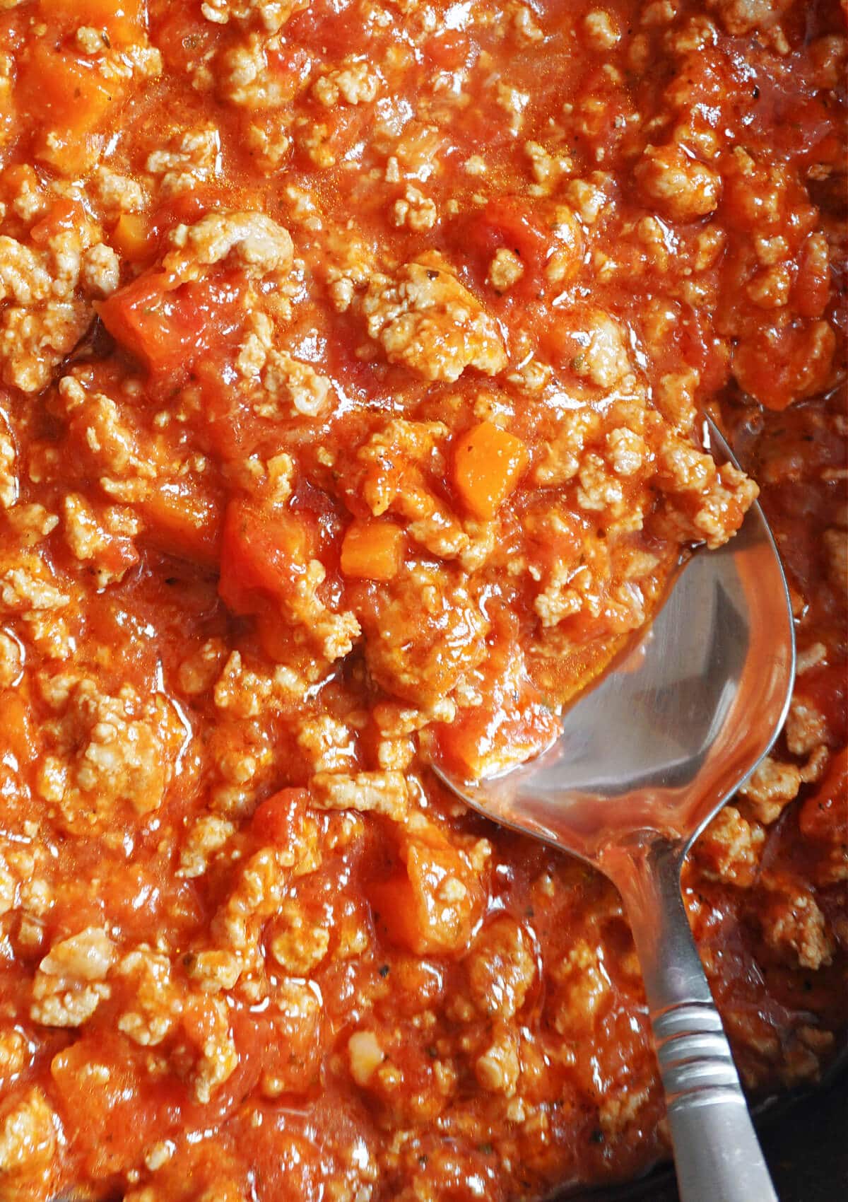 Close-up shoot of bolognese sauce with a spoon in it.