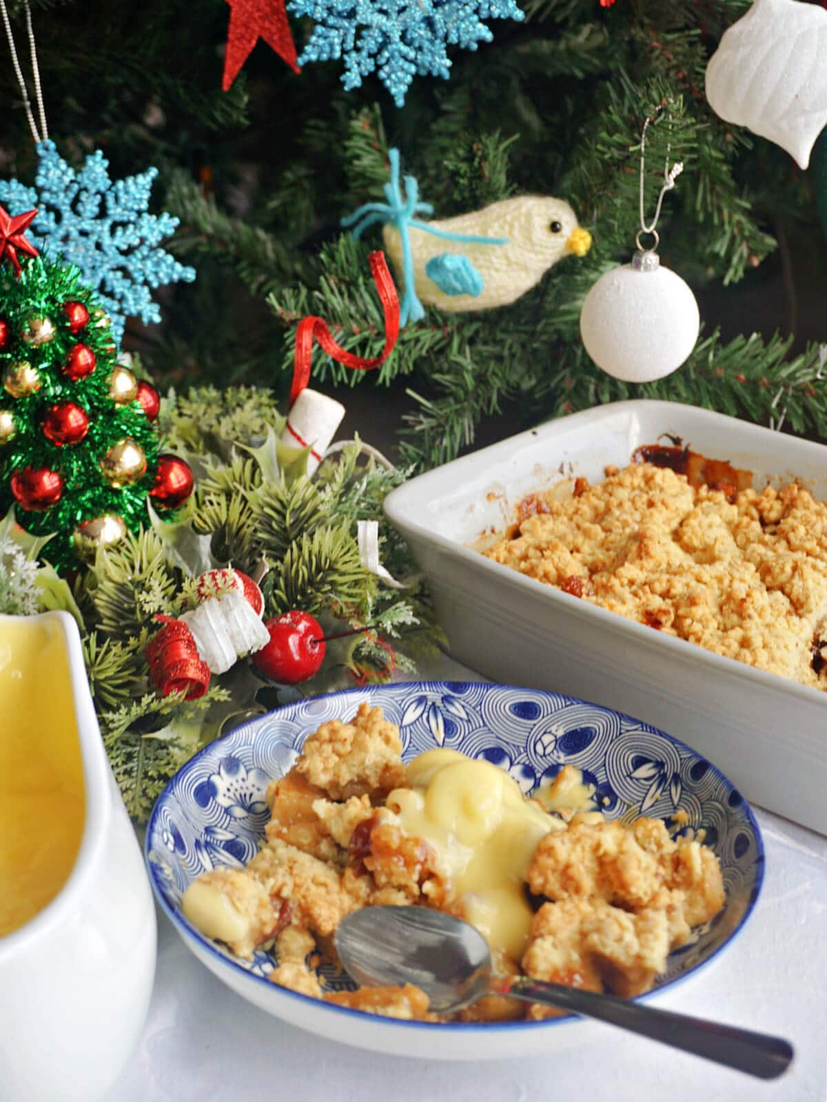 A blue plate with crumble, an oven dish with more crumble and a Christmas tree in the background.
