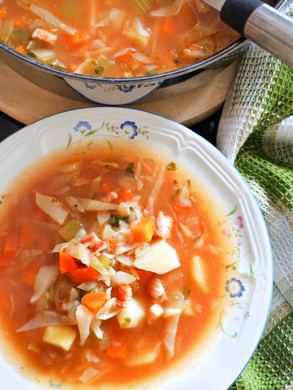 A white bowl of cabbage soup with a dish with more soup at the top.