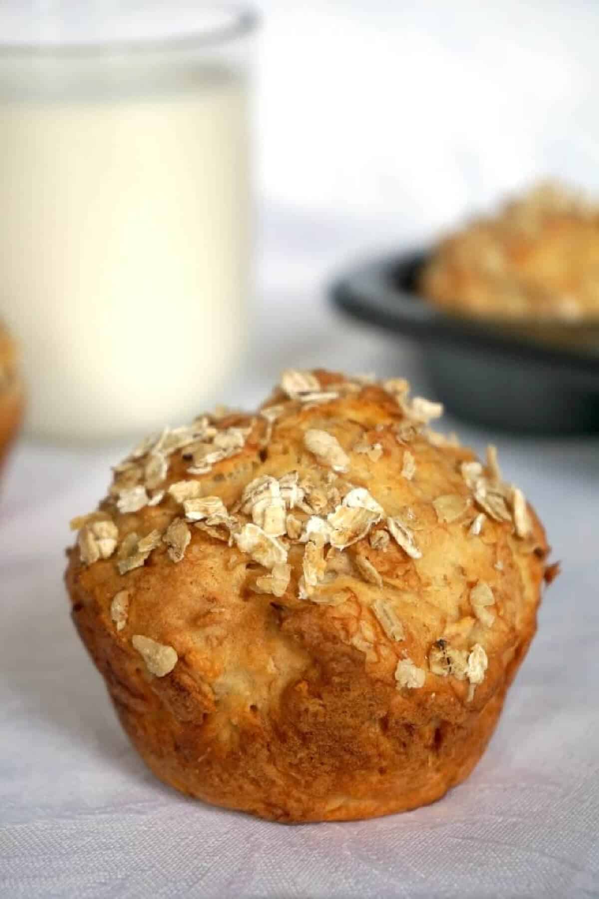 A banana muffins on a white table top with a glass of milk in the background