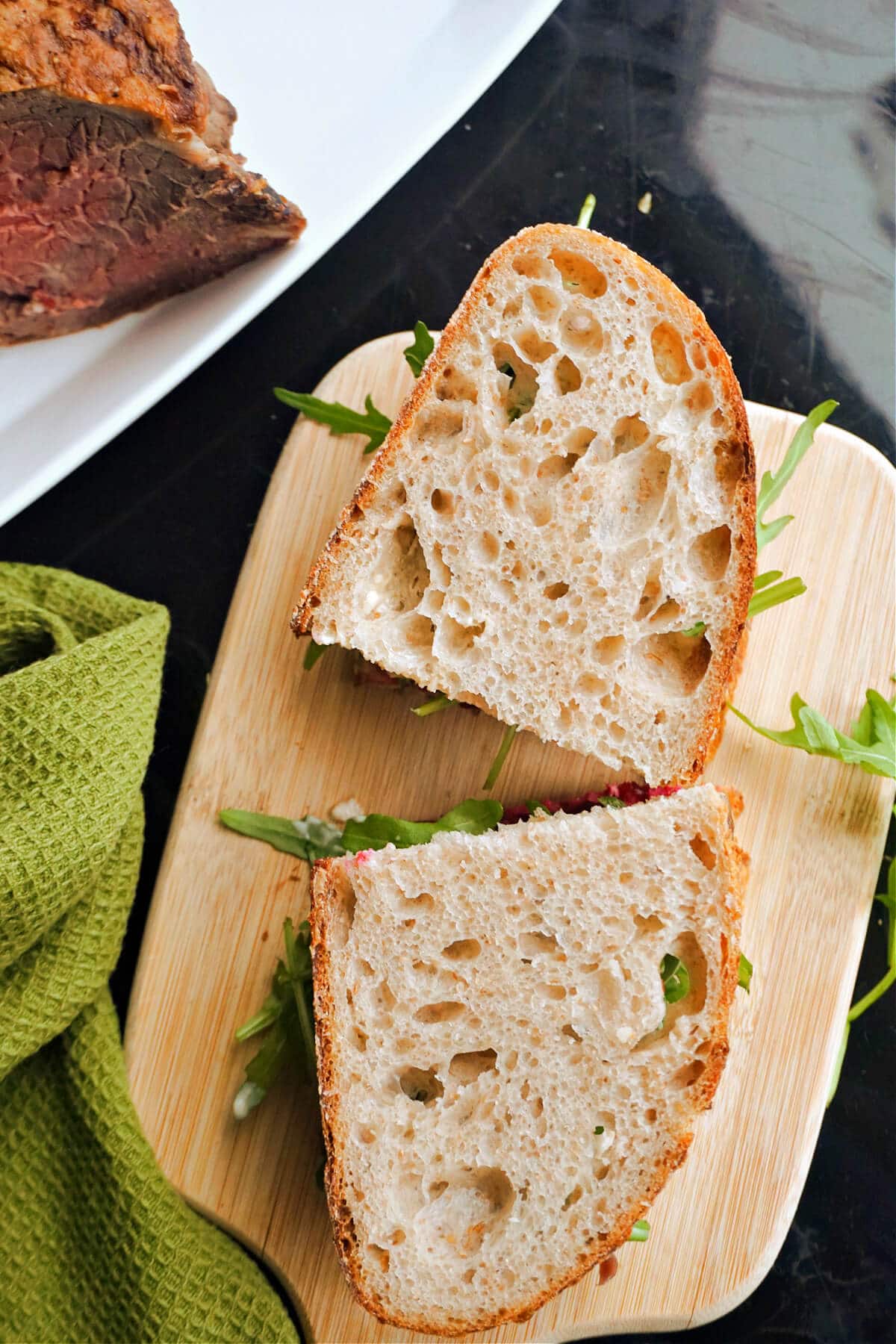 A wooden board with 2 sandwiches on.