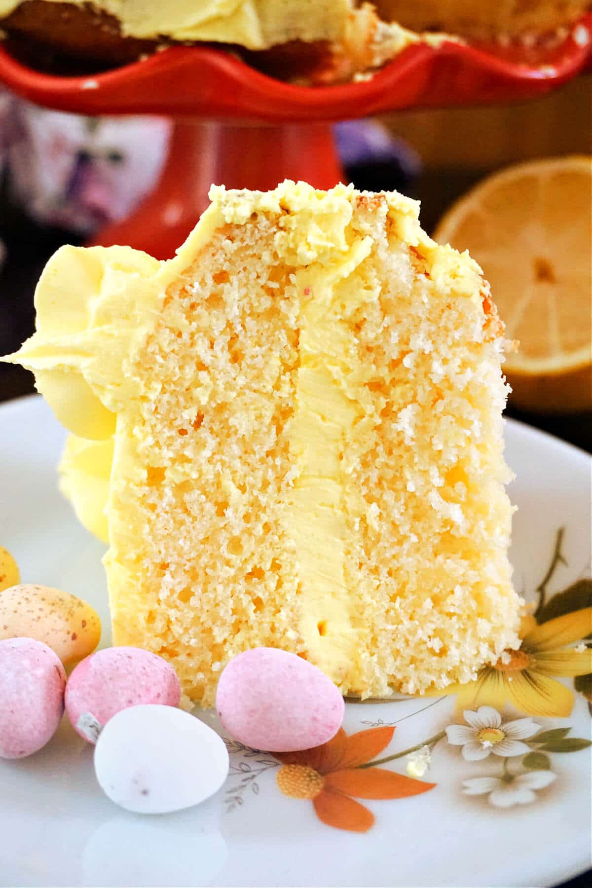 A slice of lemon cake with lemon buttercream on a white plate with mini chocolate eggs around,