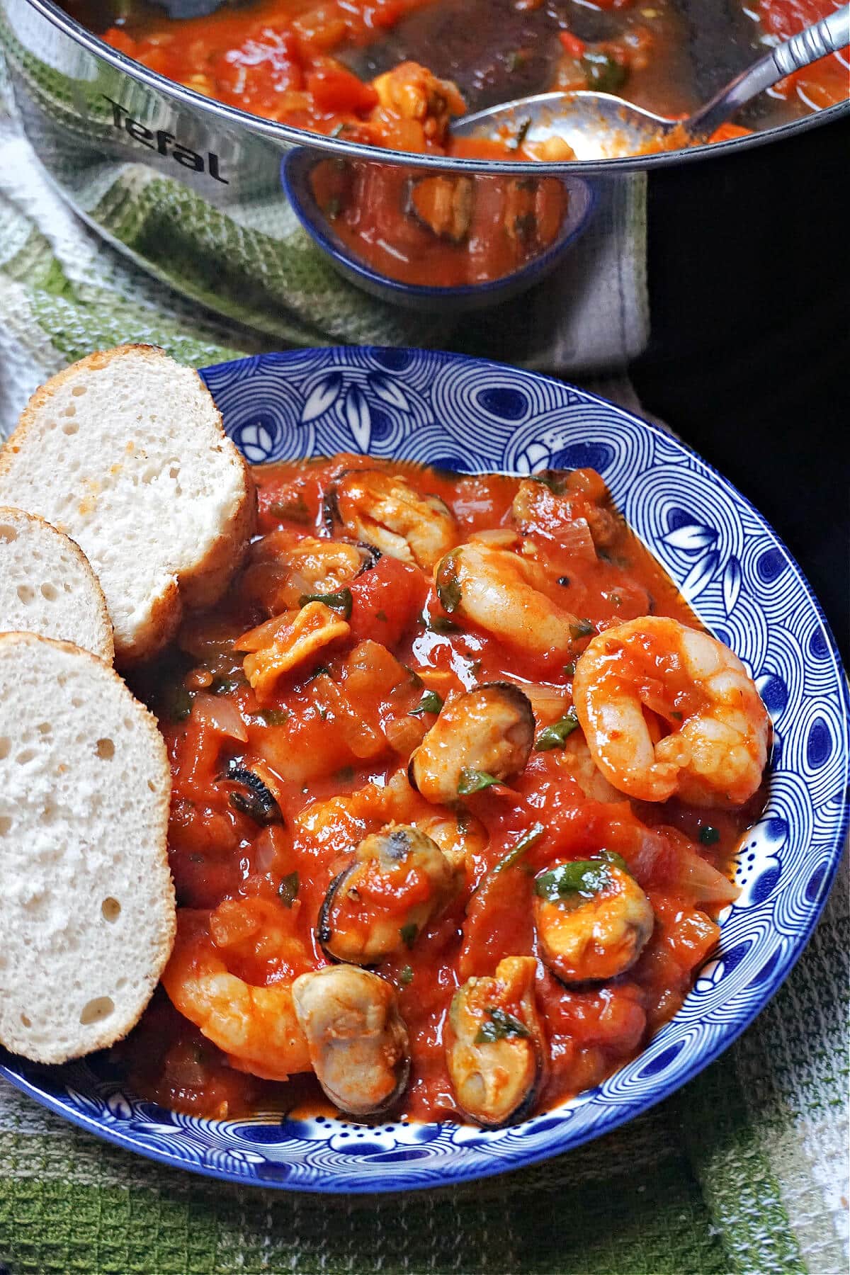 A blue bowl with seafood stew and 3 slices of bread on the side of the bowl.