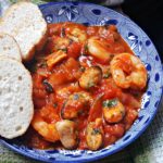 A blue bowl with seafood stew and 3 slices of bread on the side