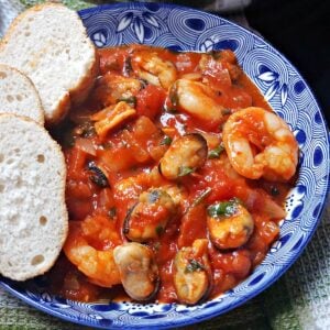 A blue bowl with seafood stew and 3 slices of bread on the side