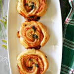 3 ham and cheese puff pastry pinwheels on a white rectangle plate.