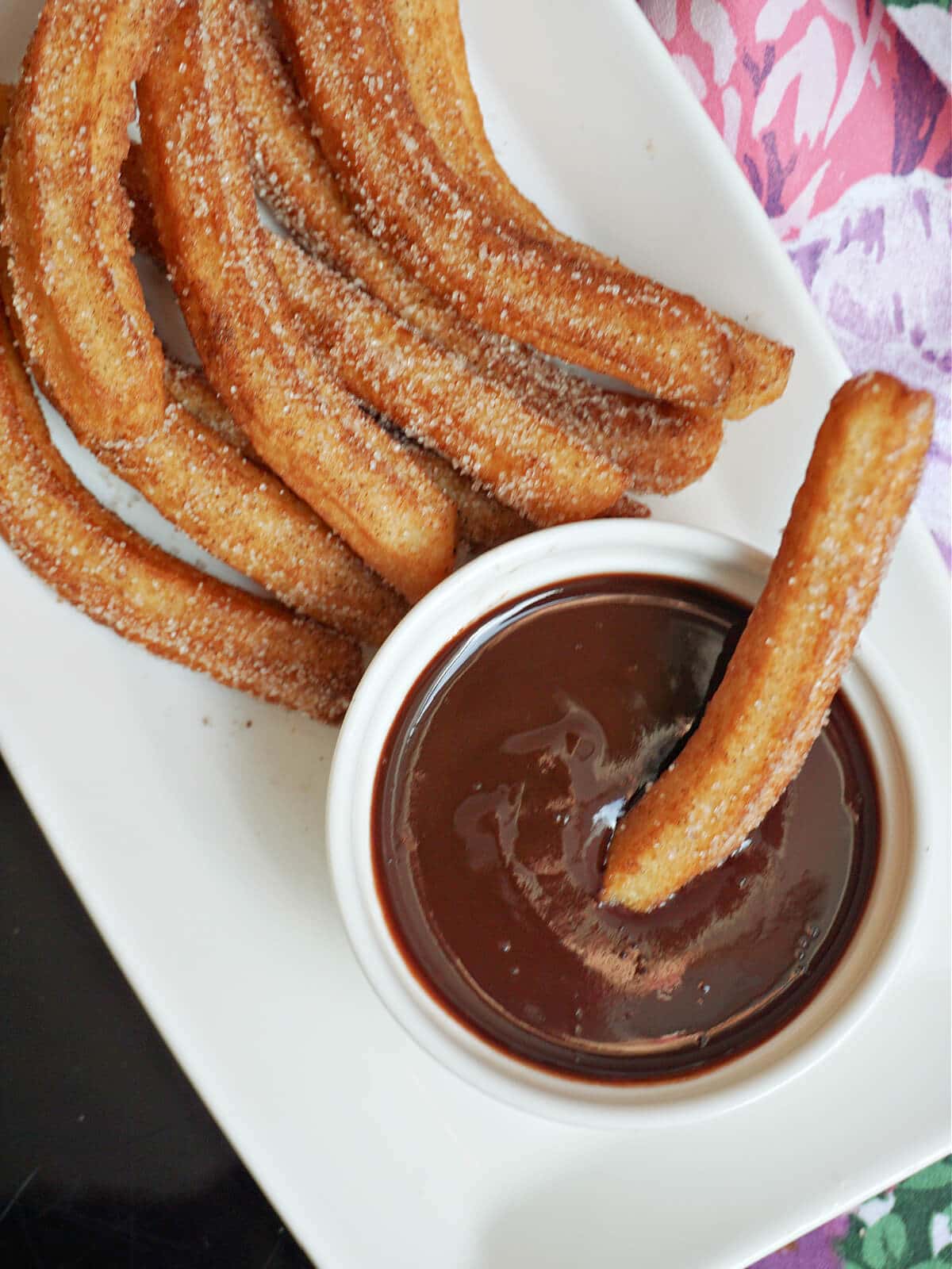 A ramekin with a churro being dipped in chocolate sauce and churros on a white plate.