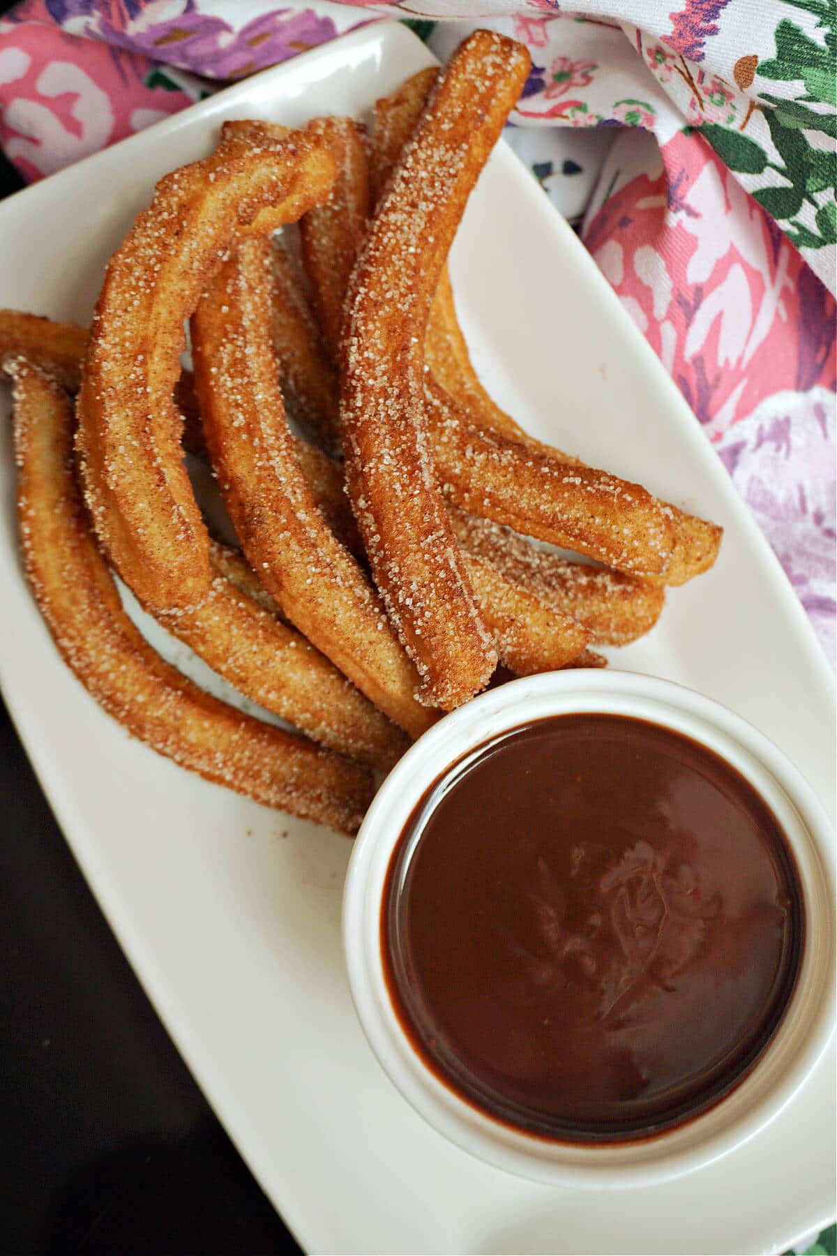 Overhead shoot of a white rectangle plate with churros and a white ramekin with chocolate sauce