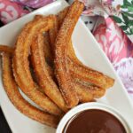 A white plate with churros and a ramekin with chocolate sauce