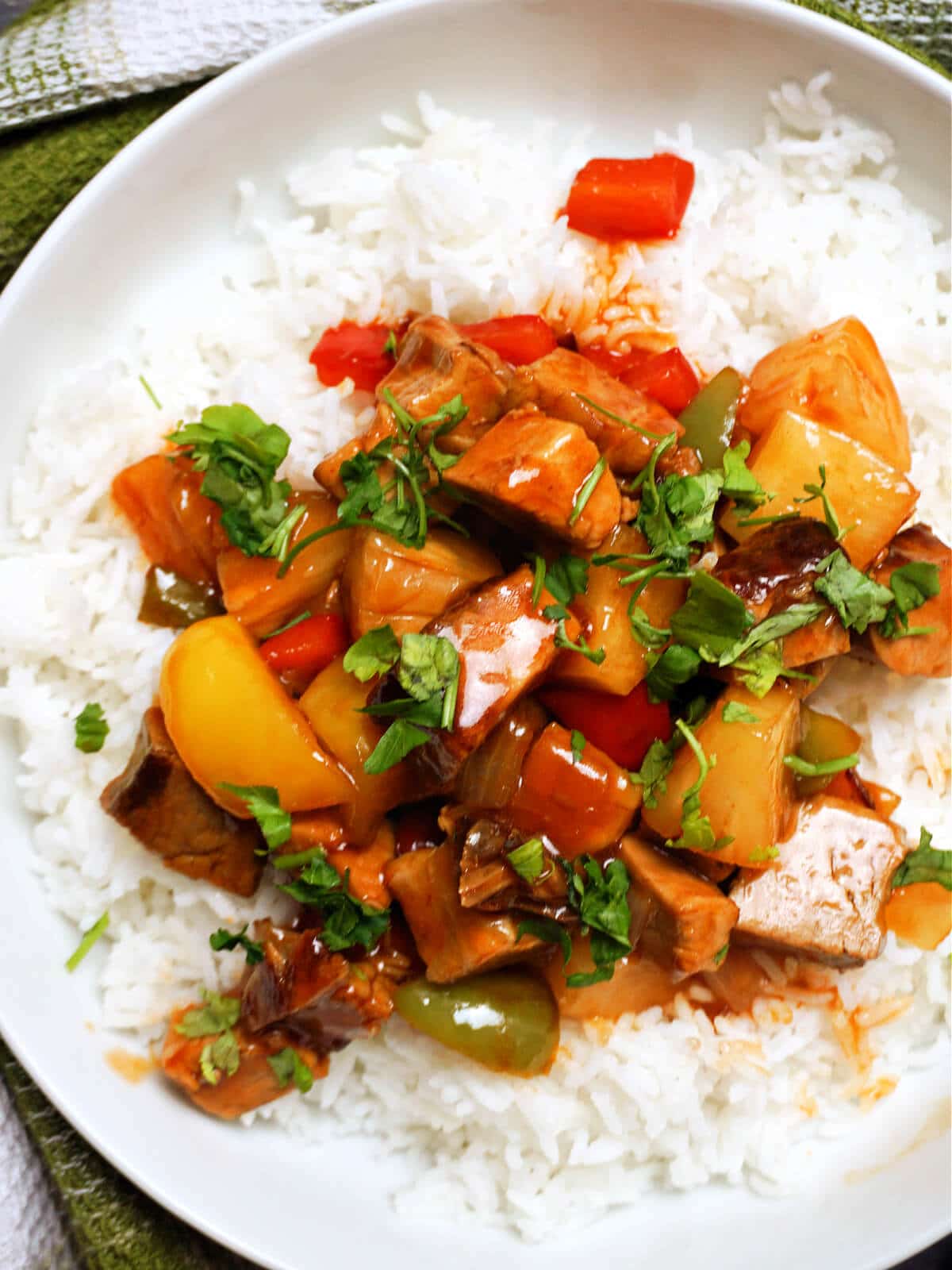 A white plate with sweet and sour pork over a bed of rice