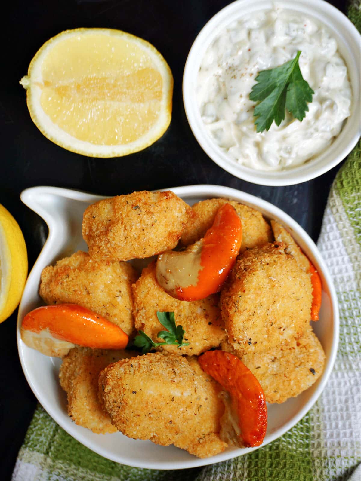 Overhead shoot of a white serving bowl with breaded scallops, a ramekin with tartar sauce and half a lemon.