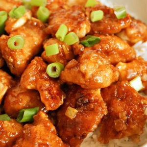 Overhead shoot of a white bowl with orange chicken pieces on a bed of rice